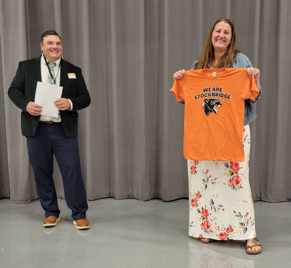 Principal Kunzelman holds up a Staff t-shirt.